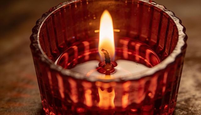 Flickering votive candle burning in red ribbed glass holder with warm melting wax glow