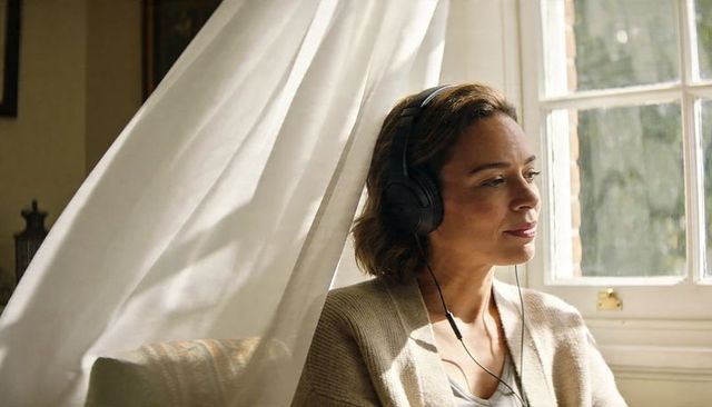 Contemplative woman wearing headphones gazing out sunlit window in cozy living room