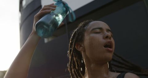 Exhausted woman pouring water on head in city