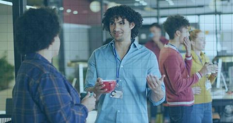 Curly man talking holding red mug in office breakroom with coworkers collaborating