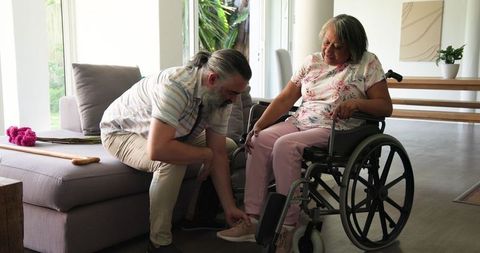 Caring man helping senior woman in wheelchair at home
