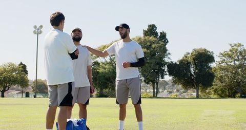 Three teammates talking and strategizing on sunny sports field with duffel bag