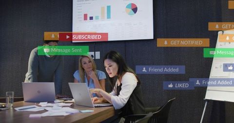Asian woman presenting laptop data with team amid social notification overlays