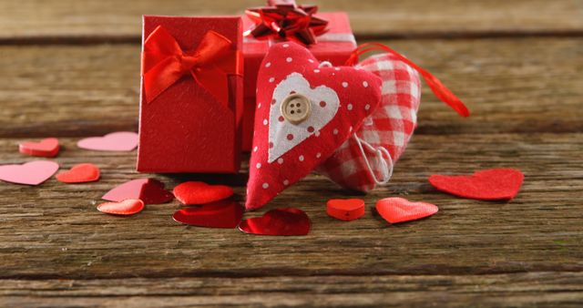 A red gift box with a bow is paired with a fabric heart, surrounded by small paper hearts on a wooden surface, symbolizing affection and gift-giving. Perfect for Valentine's Day themes, the arrangement evokes a sense of romance and celebration of love.