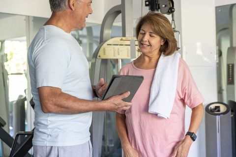 Mature couple receiving personalized fitness coaching with tablet in well-equipped gym