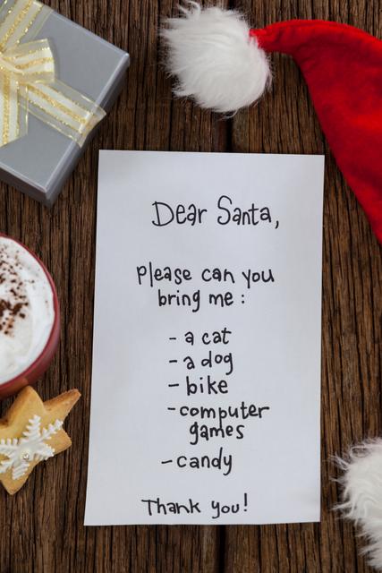 Handwritten letter to Santa Claus on wooden table, surrounded by Christmas decorations including a Santa hat, gift box, and hot chocolate. Ideal for holiday greeting cards, Christmas-themed advertisements, and festive blog posts.