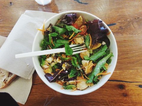 Fresh mixed greens salad with croutons and plastic fork on rustic wooden table healthy lunch bowl