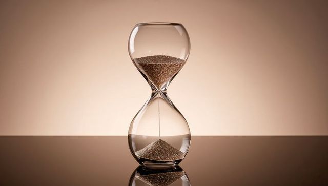 Transparent glass hourglass with flowing sand on reflective surface