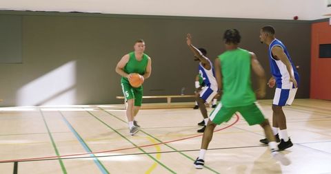 Indoor basketball game showing diverse men's teams dribbling, defending, and powering layup
