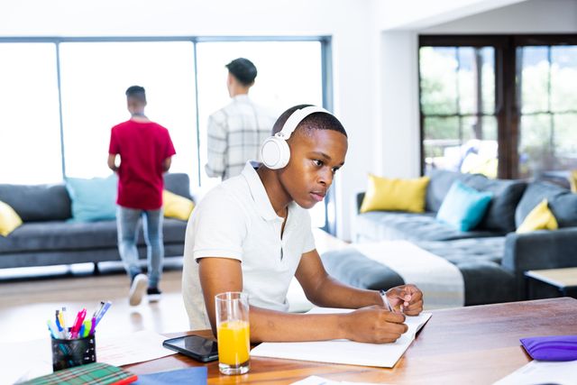 A focused teenage boy wearing headphones while studying at home. This image represents modern education practices such as e-learning and home schooling. Ideal for use in educational materials, advertisements for online learning platforms, or articles about youth lifestyle and technology in education.