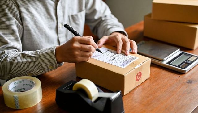 E-commerce packing: labeling shipping box on wood desk with scale, tape, pen