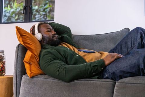 African american man relaxing on sofa listening to music with headphones and smartphone