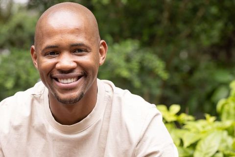 African american man smiling in garden wearing tan crewneck, closeup headshot with bokeh