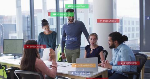 Diverse team collaborating around laptop in modern office using social media overlays