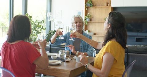Multigenerational women toasting with white wine around wooden dining table at home