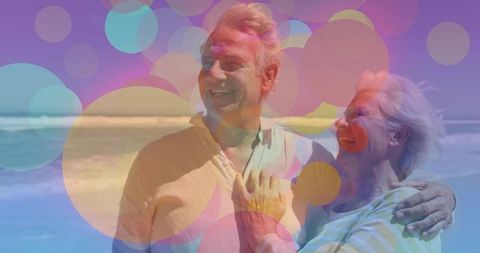 Senior Couple Embracing On Beach With Colorful Bokeh Effect