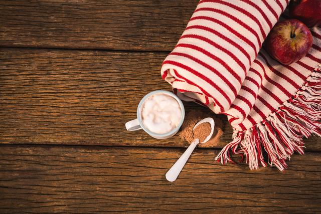 Perfect for illustrating autumn or fall themes, this image showcases a cozy setup with a striped blanket, two apples, and a coffee mug on a rustic wooden table. Ideal for use in blogs, social media posts, or advertisements related to seasonal comfort, home decor, or warm beverages.
