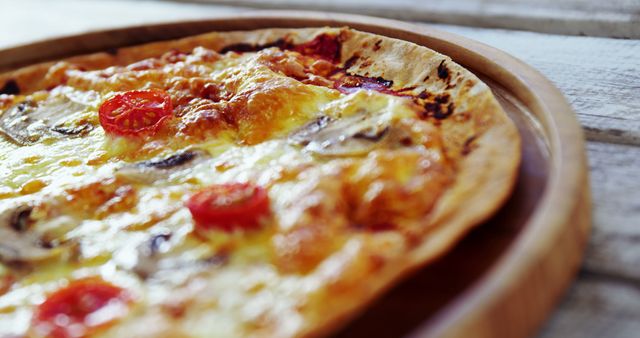 A hot, cheese-melted pizza with tomatoes and mushrooms is served on a wooden board. - Download Free Stock Photos Pikwizard.com
