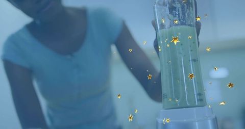 Holding blender jar pouring green smoothie with gold star sparkles in home kitchen