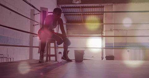 Sitting female boxer resting on stool in boxing ring, contemplative training scene