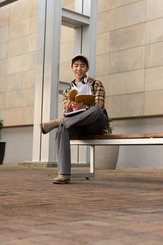 Young asian student sitting on bench reading notebook in urban plaza casual campus life