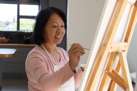 Senior asian woman painting on easel in rustic art nook