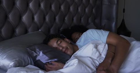 Male couple spooning at night in bedroom with tufted leather headboard and satin pillow