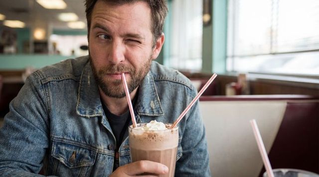 Winking bearded man sipping milkshake with whipped cream in retro diner booth
