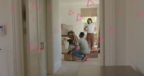 Two adults unpacking boxes in daylit hallway with pink triangle overlays showing teamwork