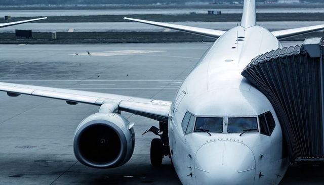 Commercial narrow-body jet docking at gate with jet bridge on overcast airport tarmac