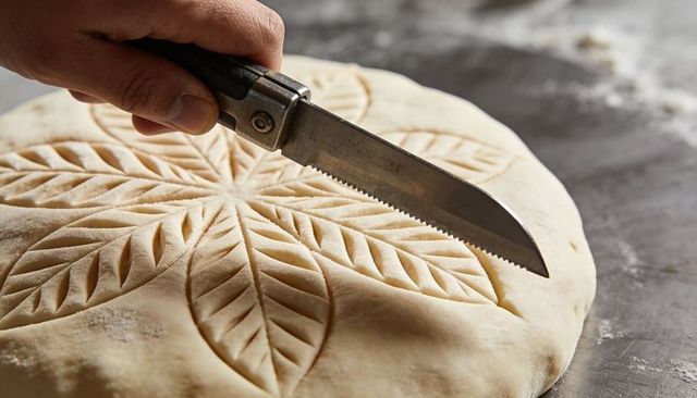 Artisan bread scoring with leaf pattern on round dough using handheld serrated blade