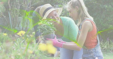 Woman teaching child planting flowers in sunny garden wearing straw hat and pink gloves