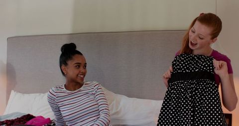 Multicultural friends trying on polka dot dress in casual bedroom fashion moment