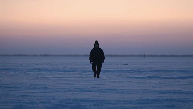 Solitary silhouette walking across vast frozen plain at pastel sunrise horizon, winter dawn