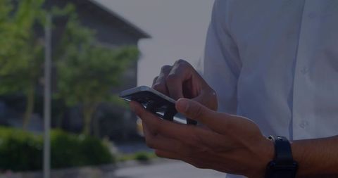 Man Using Smartphone in Sunlit Suburban Street Wearing Business Attire