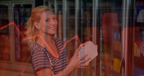 Smiling woman holding product box in supermarket aisle with downward sales graph overlay