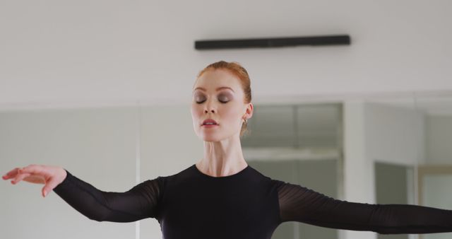 Female ballet dancer practicing with focus and elegance in a dance studio. She's wearing a black leotard, highlighting her performance and fitness routine. Ideal for content related to dance, performing arts, fitness, dedication, and elegance.