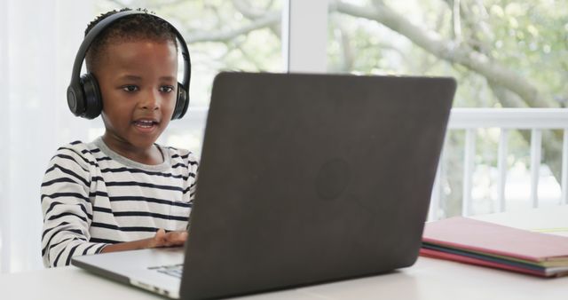 Happy african american boy having school laptop video call and wearing headphones at home. Domestic life, education and technology, unaltered.