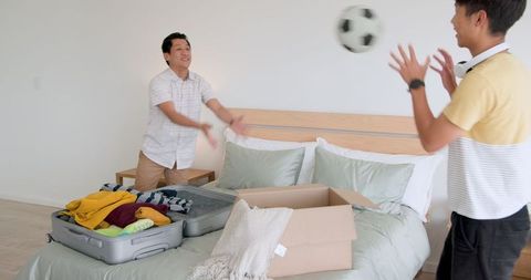 Two Men Packing Suitcase for Vacation in Relaxed Bedroom Setting