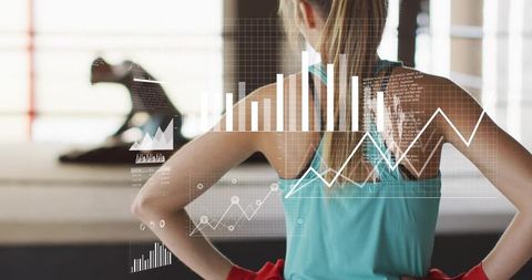 Woman tracking fitness metrics while observing trainer in bright gym studio
