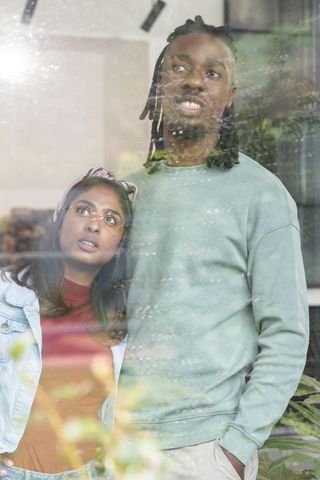 Diverse couple standing at cafe window with reflections, intimate urban lifestyle portrait