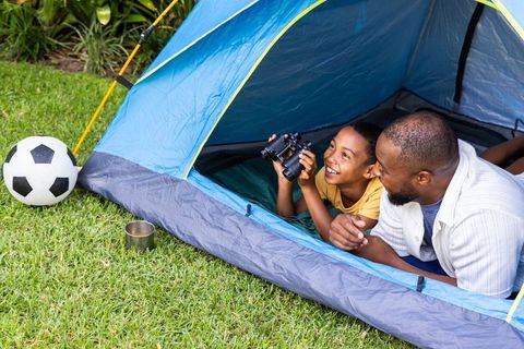 African american father and son backyard camping laughing and birdwatching with binoculars