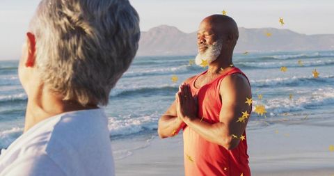 Older man meditating on beach at golden hour pressing palms in prayer for mindful wellness