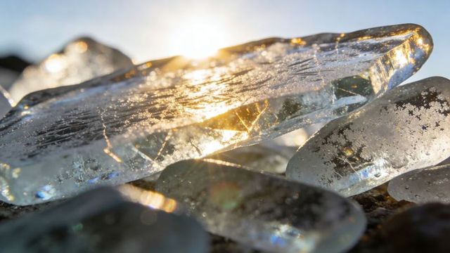 Shimmering ice shards refracting golden sunlight over pebble beach with crystal facets