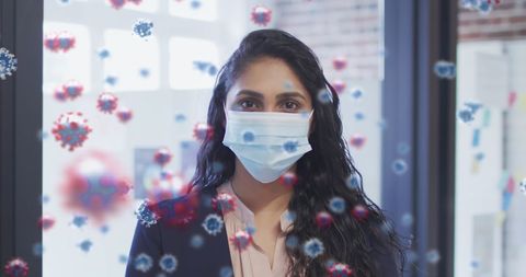 Woman wearing face mask with floating covid-19 particles in office