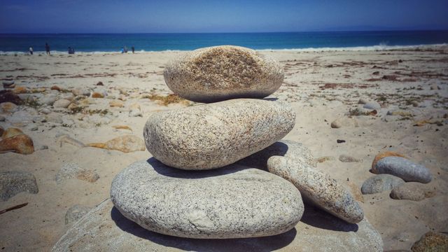 Stone stack on sandy beach with ocean in the background. Ideal for use in wellness, relaxation, and meditation themes. Suitable for promoting beach destinations and outdoor activities. Perfect for websites, brochures, and posters focused on nature and tranquility.