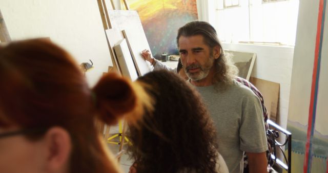 Group of artists collaborating in a spacious art studio, with focus on experienced artist. Discussion about project visible. Use for themes of teamwork, creativity, artistic process, collaboration, and brainstorming sessions in professional settings.