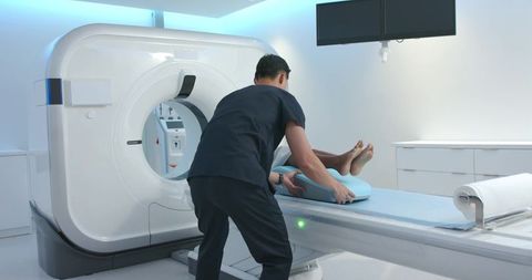 Asian technician positioning african american female patient for ct scan in modern radiology room