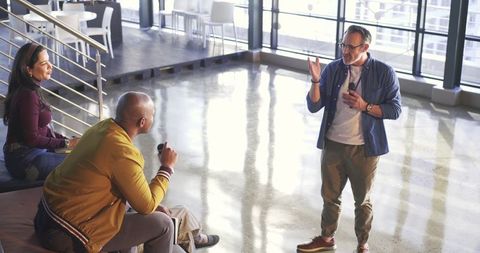 Mature leader presenting and gesturing in modern coworking atrium, engaging team
