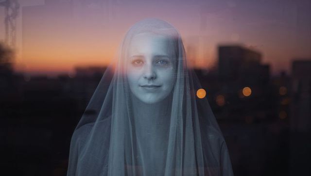 Reflective woman in veil at sunset with cityscape backdrop